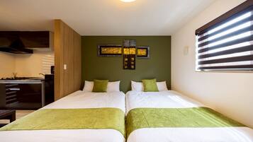 Habitación de hotel con dos camas, kitchenette y un amplio ventanal con persianas.