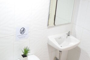 Un baño con lavamanos blanco, un espejo y un cartel con el símbolo de una mano.