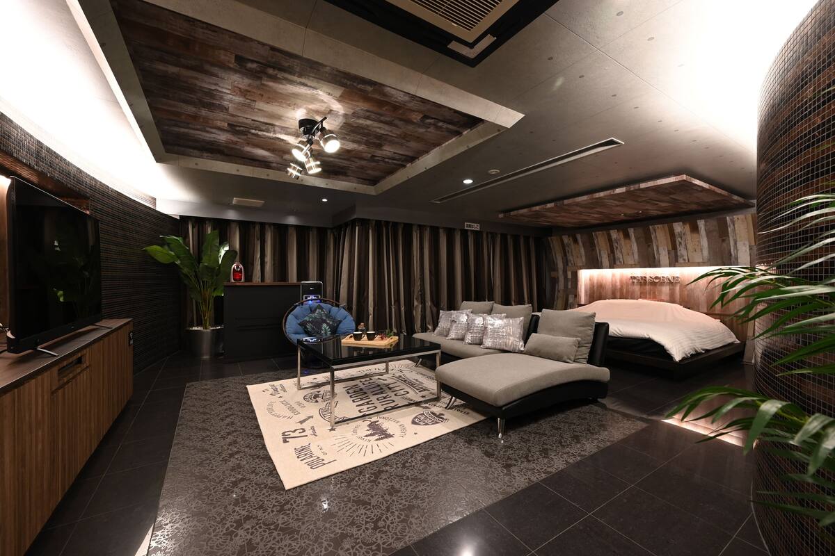 A modern bedroom with a large bed, a sofa, a desk with a laptop, and a TV.
