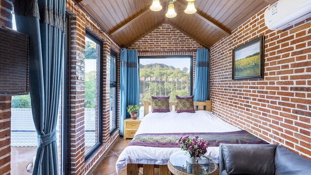 Un dormitorio con una cama grande, techo de madera, pared de ladrillo y vistas al exterior.