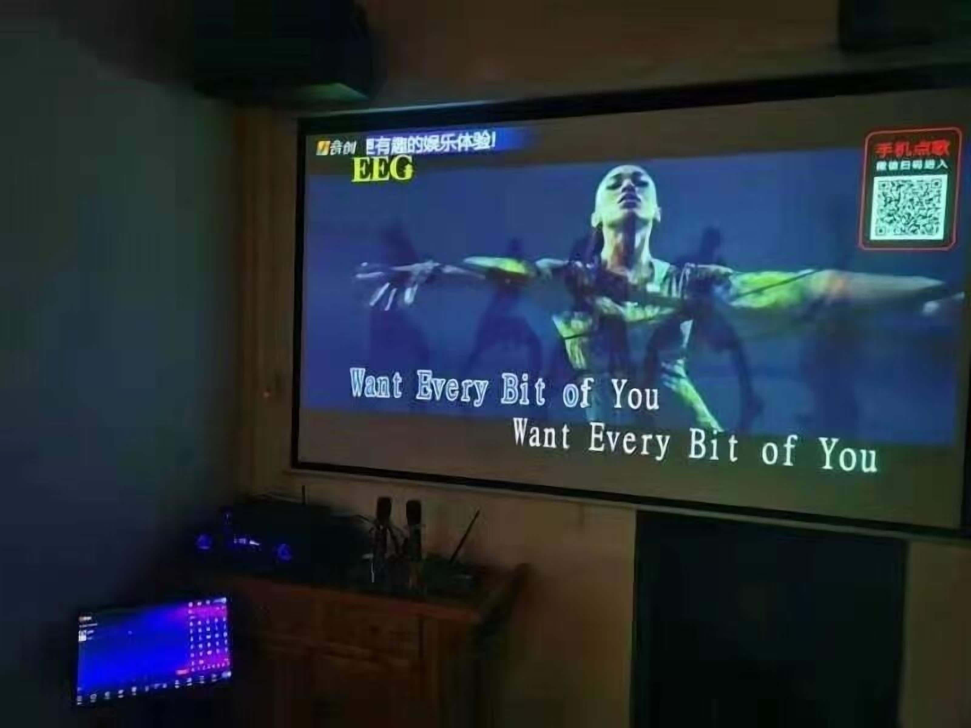 Un écran de projection diffusant un clip vidéo avec les paroles de la chanson « Want Every Bit of You » et un code QR dans le coin supérieur droit.