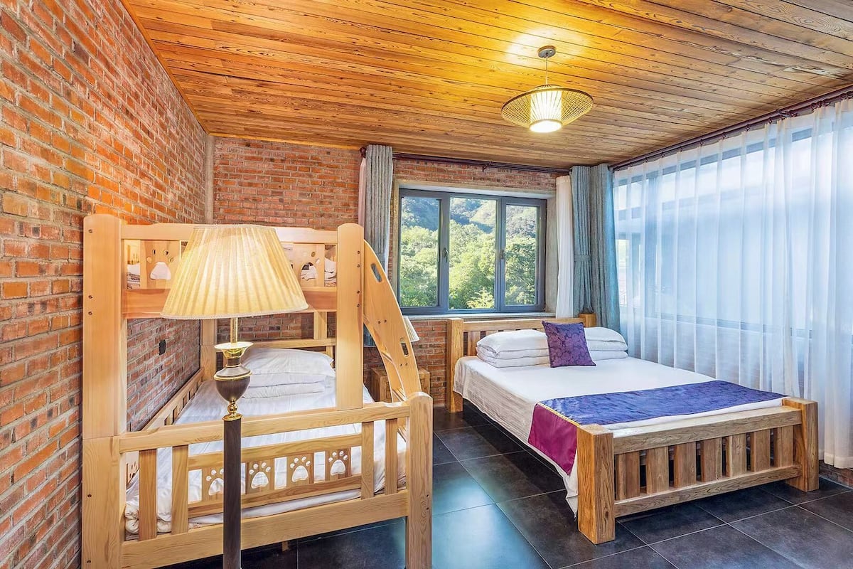 Una habitació amb dos llits de fusta, una paret de maó, una finestra gran amb cortines i un sostre de fusta.