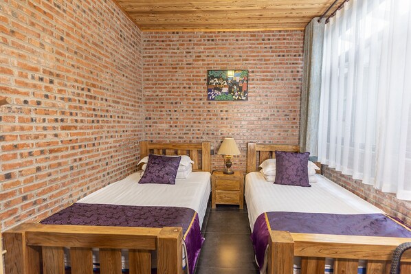 Um quarto com duas camas de madeira, uma parede de tijolos, teto de madeira e um quadro na parede.