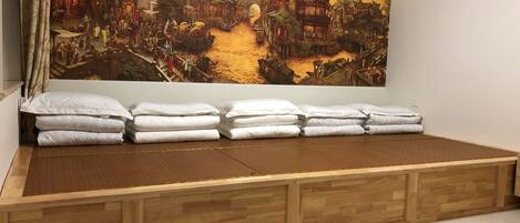 Una habitación con un mural tradicional chino, una cama con base de madera y almohadas, y un equipo de aire acondicionado en la pared.