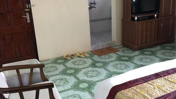 A hotel room with a bed, a wooden wardrobe, a television, a fan, a shower, and a door.