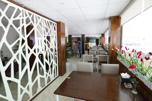 Um saguão de hotel com uma mesa de recepção de madeira, um divisório decorativo branco e uma fileira de tulipas artificiais.