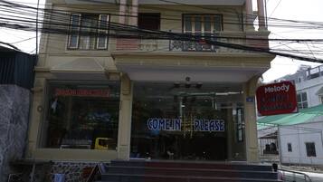 Una entrada de hotel con un cartel que dice 'COME IN PLEASE', un cartel de 'Melody Coffee Breakfast' y un cartel de 'HOANG NGOC HOTEL'.