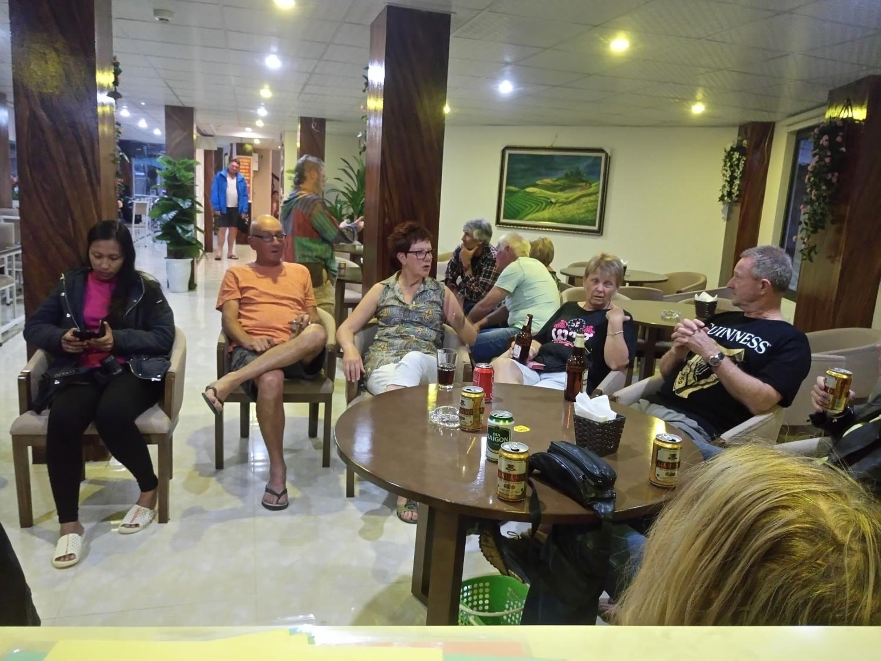 A group of people seated around a table in a well-lit indoor space with wooden pillars and a painting on the wall.