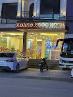 Exterior do Hotel Hoang Ngoc, com um carro e uma scooter estacionados em frente.