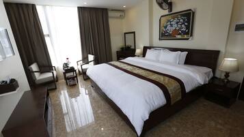 A hotel room with a large bed, a desk, a chair, a nightstand, and a painting on the wall.