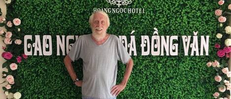 Un hombre de pie frente a un muro verde con un cartel que dice "H&N Hoang Ngo Hotel".