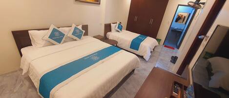 Une chambre d’hôtel avec deux lits, chacun recouvert d’une couvre-lit bleue et agrémenté d’oreillers assortis. On y trouve une armoire, un miroir et une petite table sur laquelle sont posés une télécommande et une bouteille d’eau.