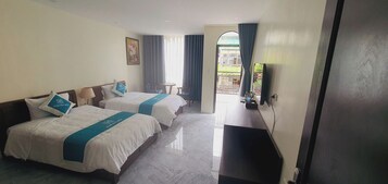 Quarto de hotel com duas camas, uma mesa pequena, uma cadeira, televisão e varanda com vista.