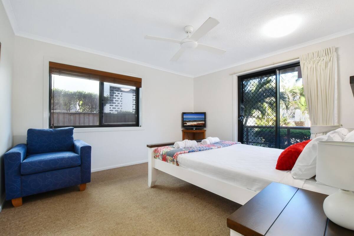 A bedroom with a bed, a chair, a television, and a ceiling fan.