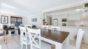 Une cuisine moderne avec des meubles blancs, un îlot central et un coin repas comprenant des chaises blanches et une table en bois.