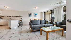 A modern living area with a grey sofa, a glass coffee table, and a kitchen in the background. - Beachport (Mooloolaba)