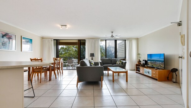 A spacious living room with a dining area, a sofa, a TV, and a balcony with a view. - Beachport (Mooloolaba)
