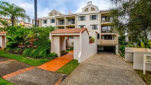 A multi-story residential building with a central courtyard, surrounded by lush greenery and a paved walkway. - Beachport (Mooloolaba)
