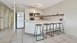 A modern kitchen with a central island, bar stools, a microwave, oven, and a refrigerator. - Beachport (Mooloolaba)