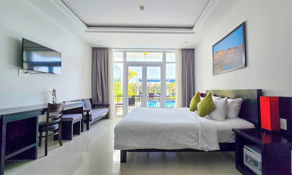 A hotel room with a bed, a desk, a TV, and a balcony with a pool view. - Riverside White House Boutique Hotel (Da Nang)