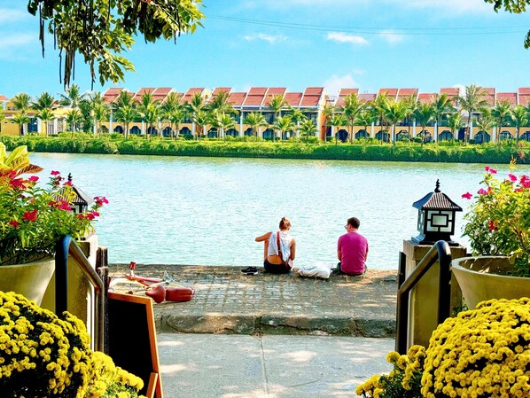 A riverside view with a row of buildings, a bridge, and people sitting by the water. - Riverside White House Boutique Hotel (Da Nang)