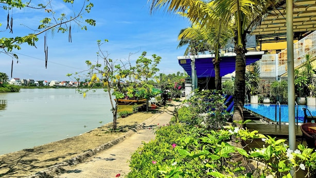 A waterfront property with a swimming pool, lush greenery, and a view of the water.