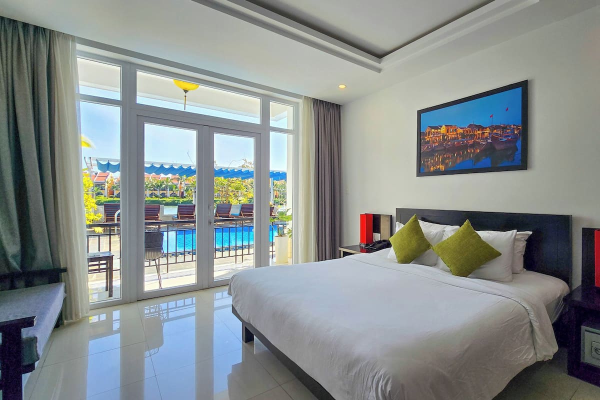 A hotel room with a large bed, a painting, and a view of a pool and outdoor area.