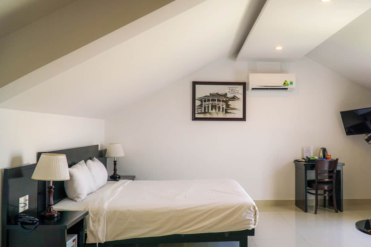 A hotel room with a bed, bedside lamps, a desk with a chair, a flat-screen TV, and a framed picture on the wall.