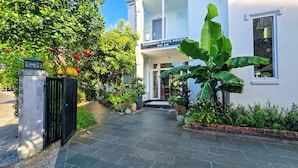 A hotel entrance with a paved pathway leading to the door, surrounded by lush greenery and potted plants.