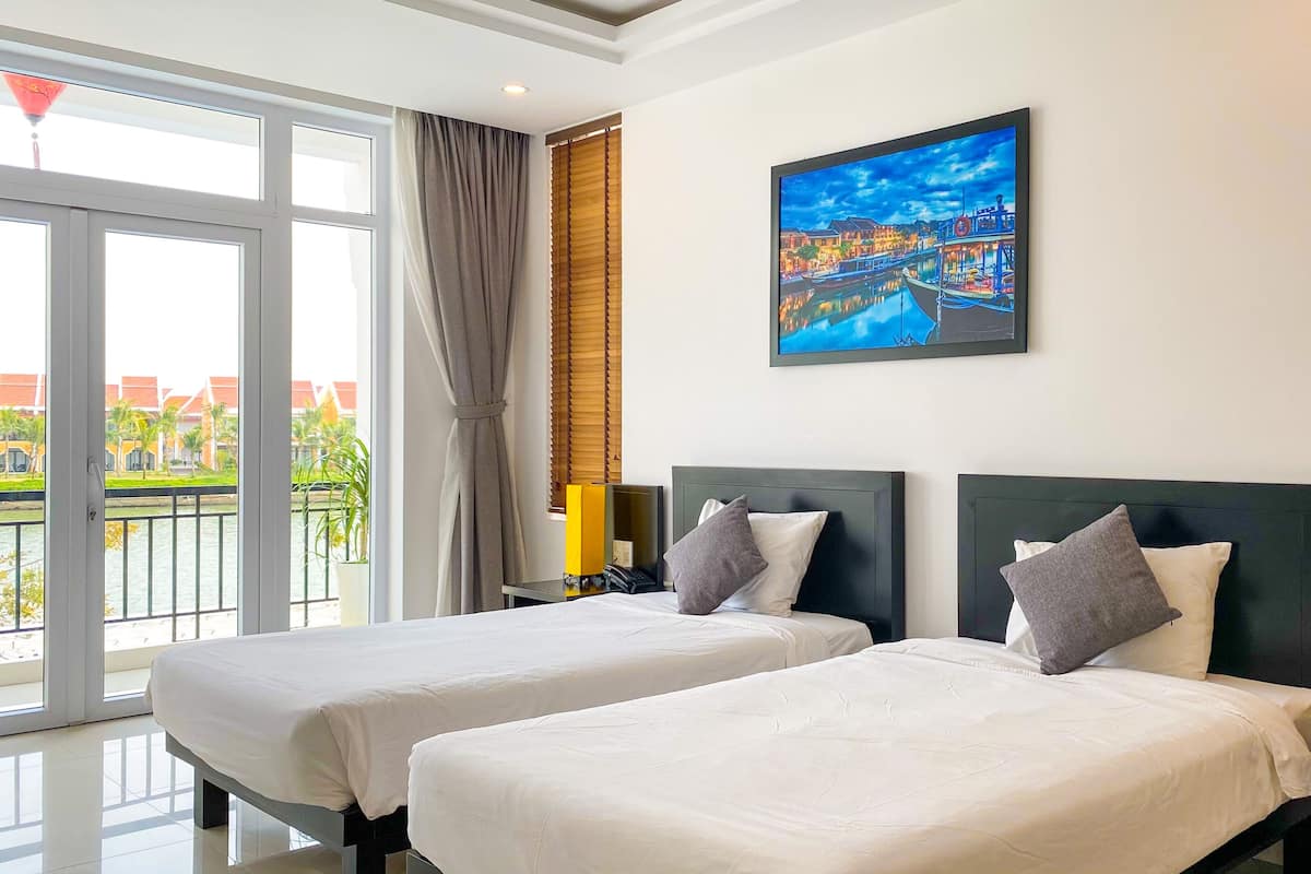 A hotel room with two beds, a large window with a view of a cityscape, and a painting on the wall.