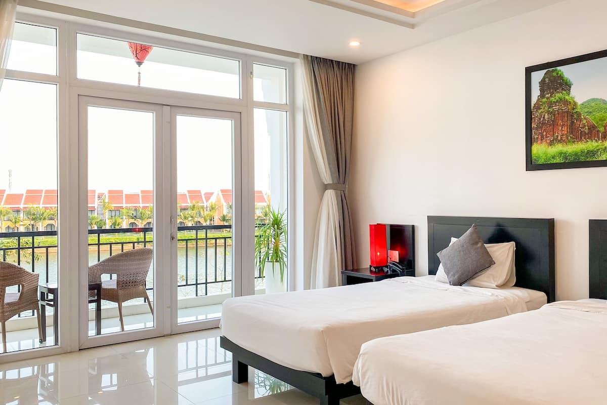 A hotel room with two beds, a large window with a view of a building and palm trees, and a balcony with wicker chairs.