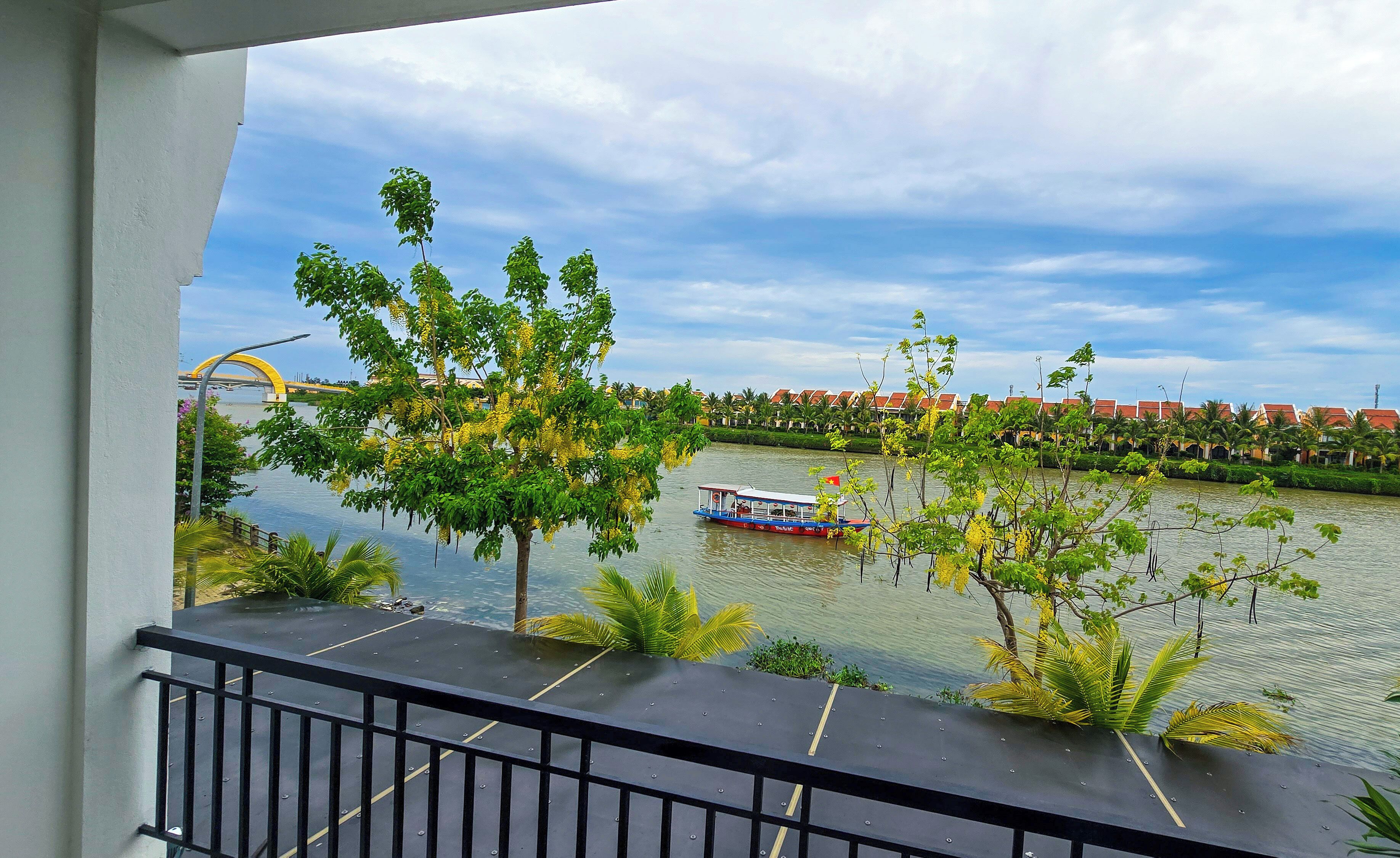 A balcony with a view of a river, a boat, and a row of houses in the background.