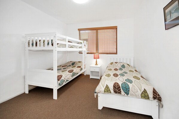 A room with bunk beds, a nightstand, a lamp, and a window with blinds.