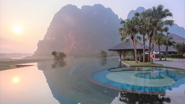A serene infinity pool with a clear view of the mountains and a thatched-roof structure.