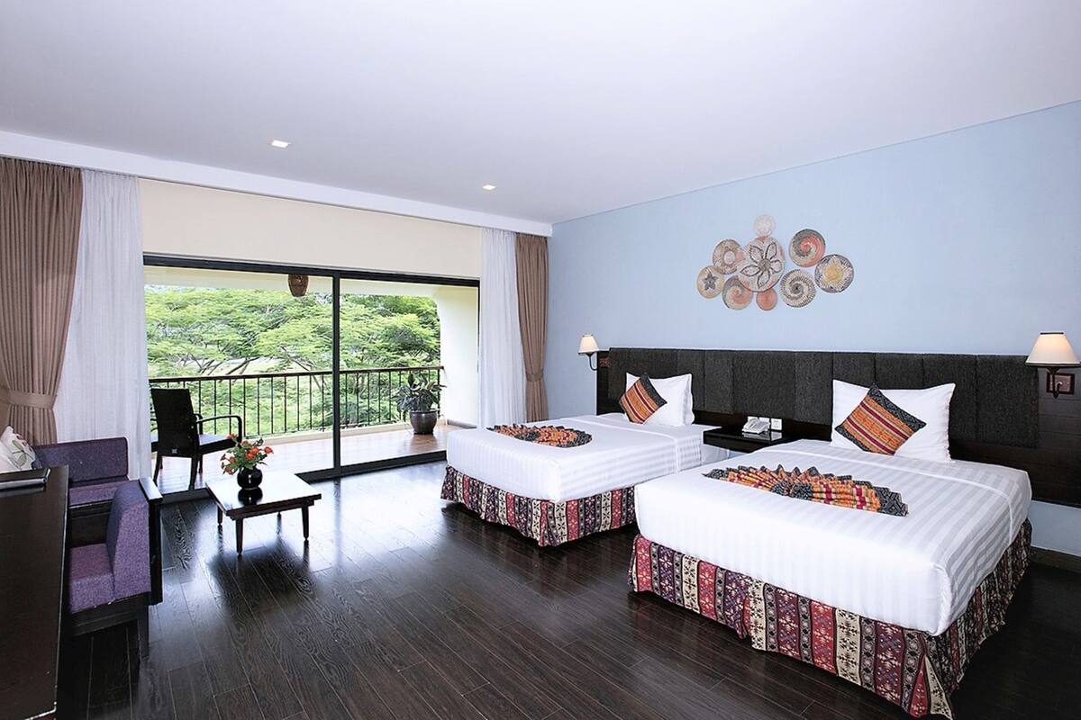A hotel room with two beds, a balcony, and a view of greenery.