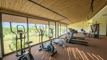 A gym with exercise equipment and large windows overlooking a garden.