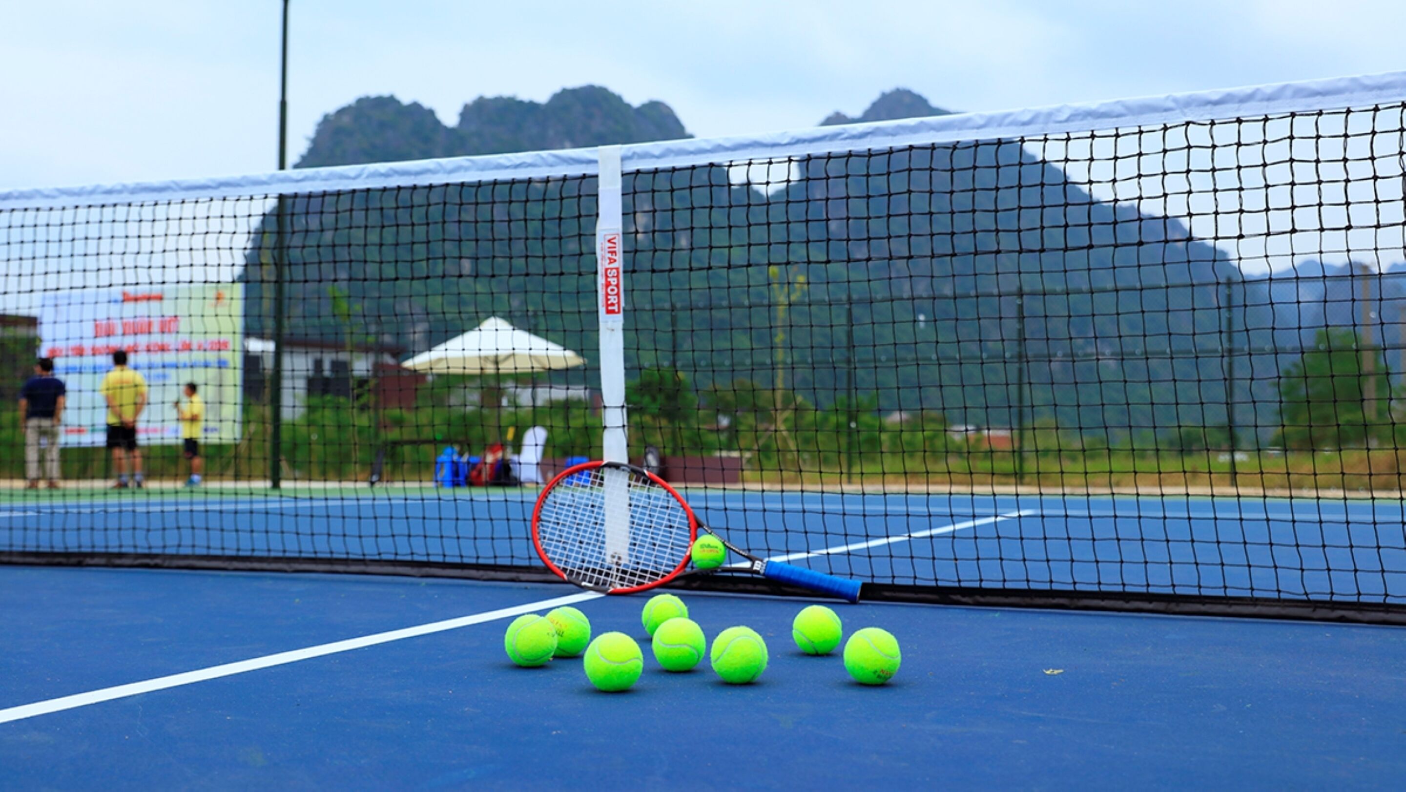 Una cancha de tenis con una red, raquetas y varias pelotas.