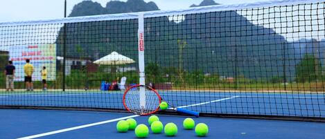 Una cancha de tenis con una red, raquetas y varias pelotas.