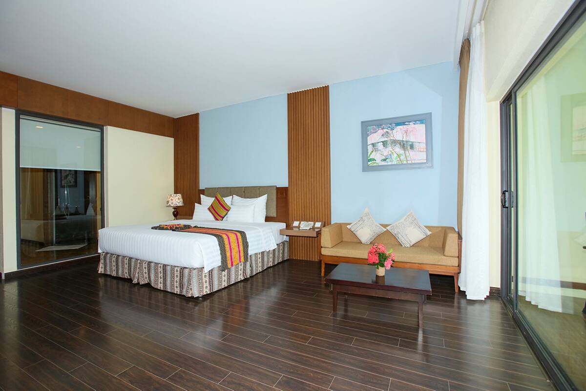 A hotel room with a large bed, a sofa, a coffee table, and a painting on the wall.