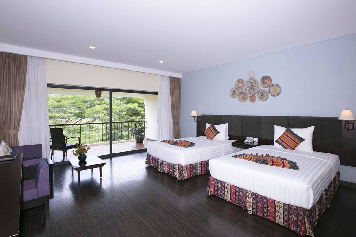A hotel room with two beds, a balcony, and a view of greenery.