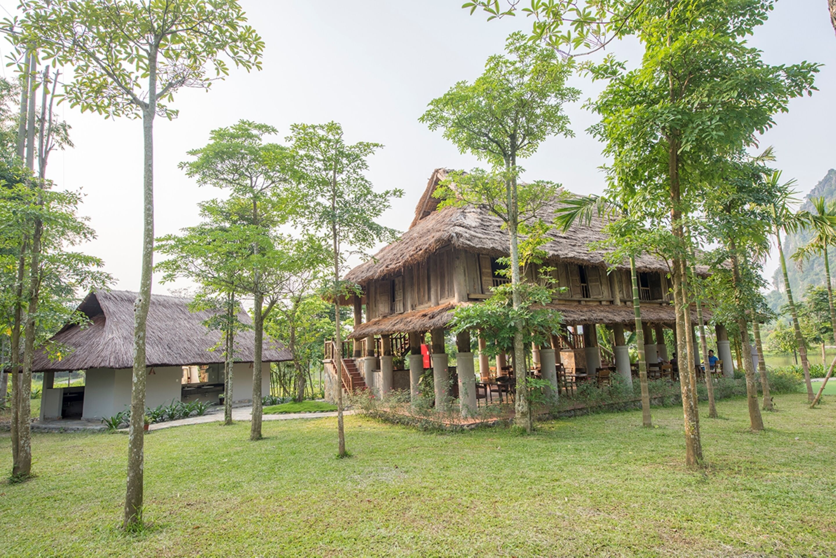 Ein rustikales Holzhaus mit Strohdach, umgeben von üppigem Grün und Bäumen.