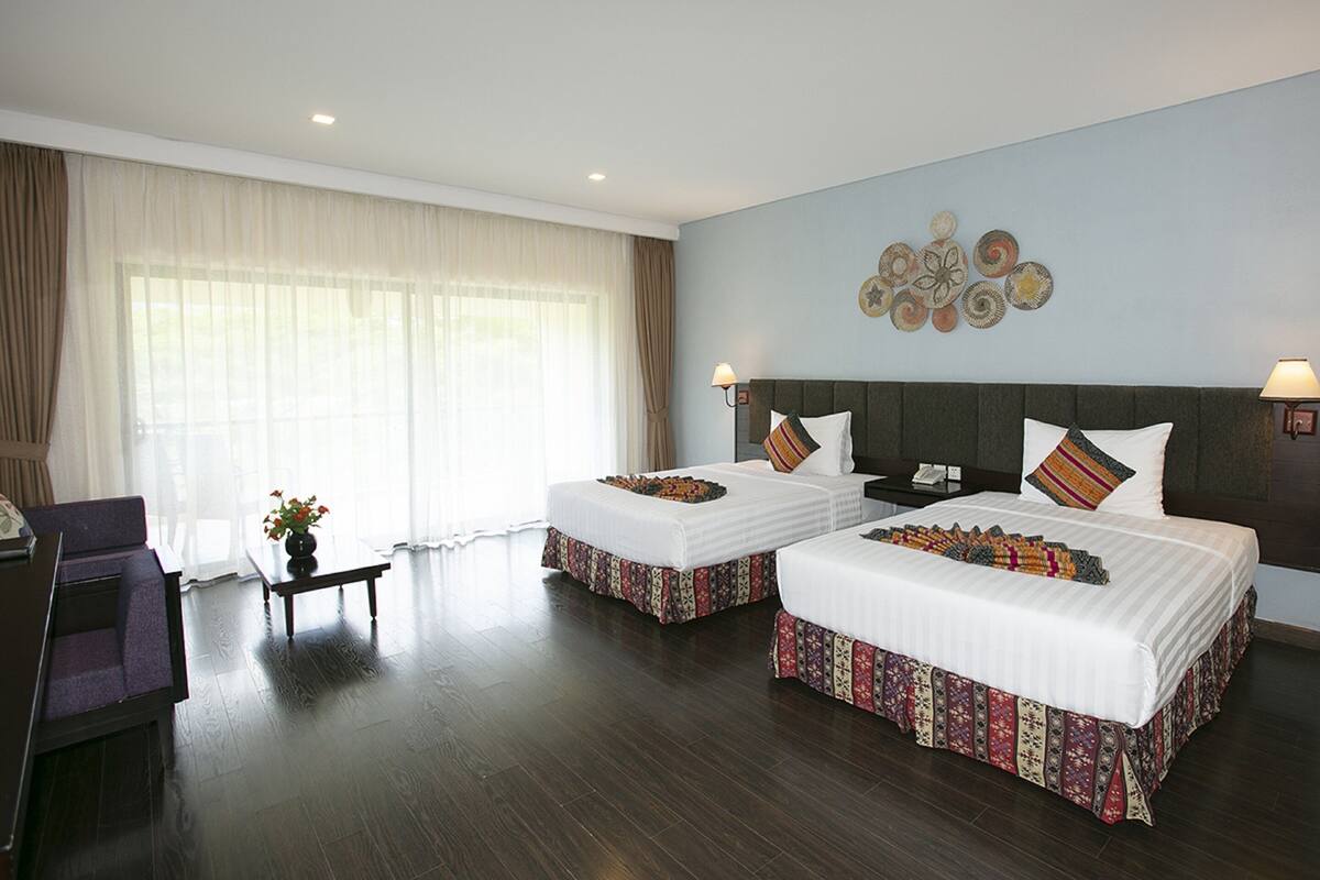 A hotel room with two beds, a desk, a chair, and a window with curtains.