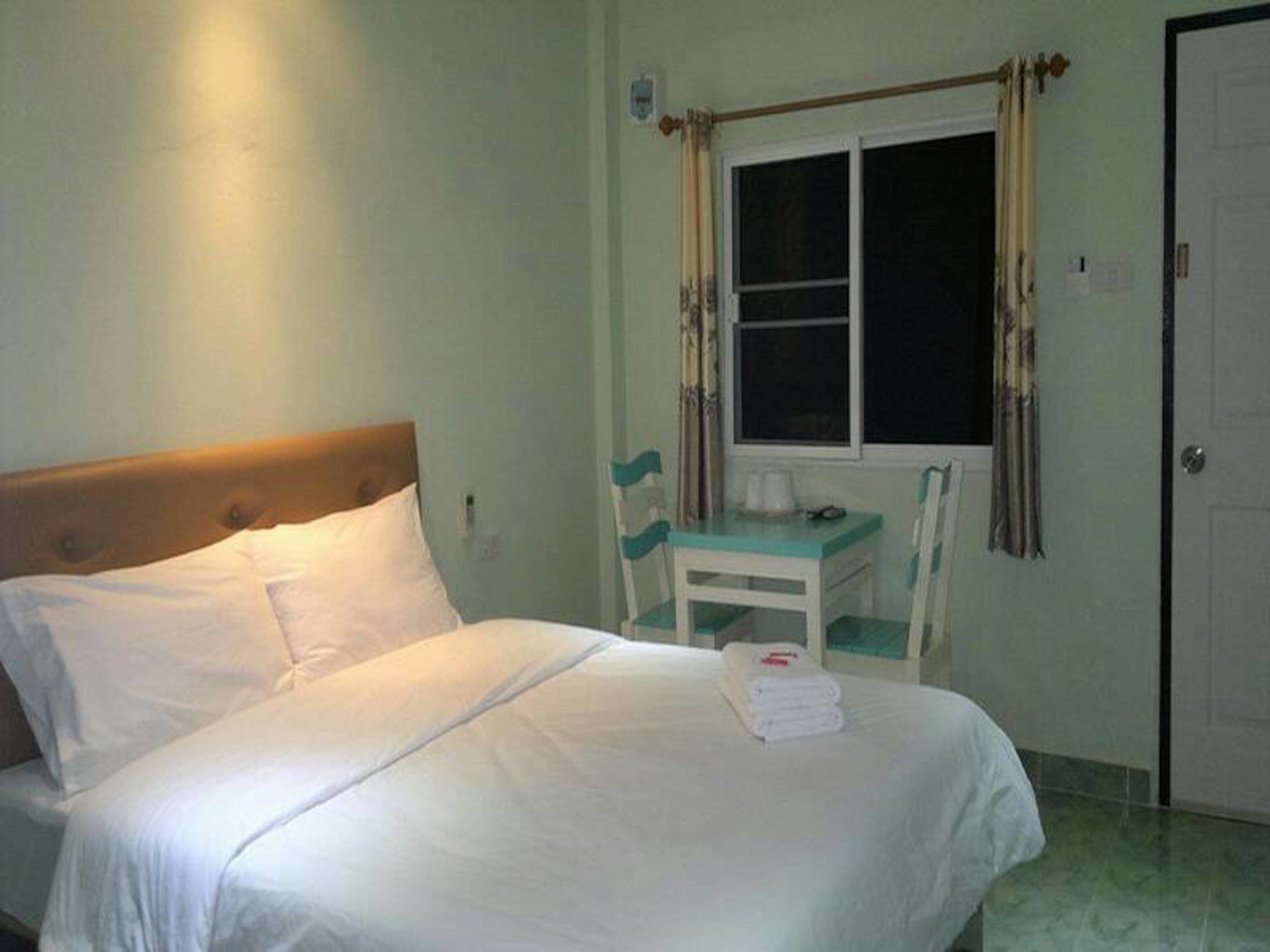 A bedroom with a bed, a small table with chairs, a window with curtains, and a door.