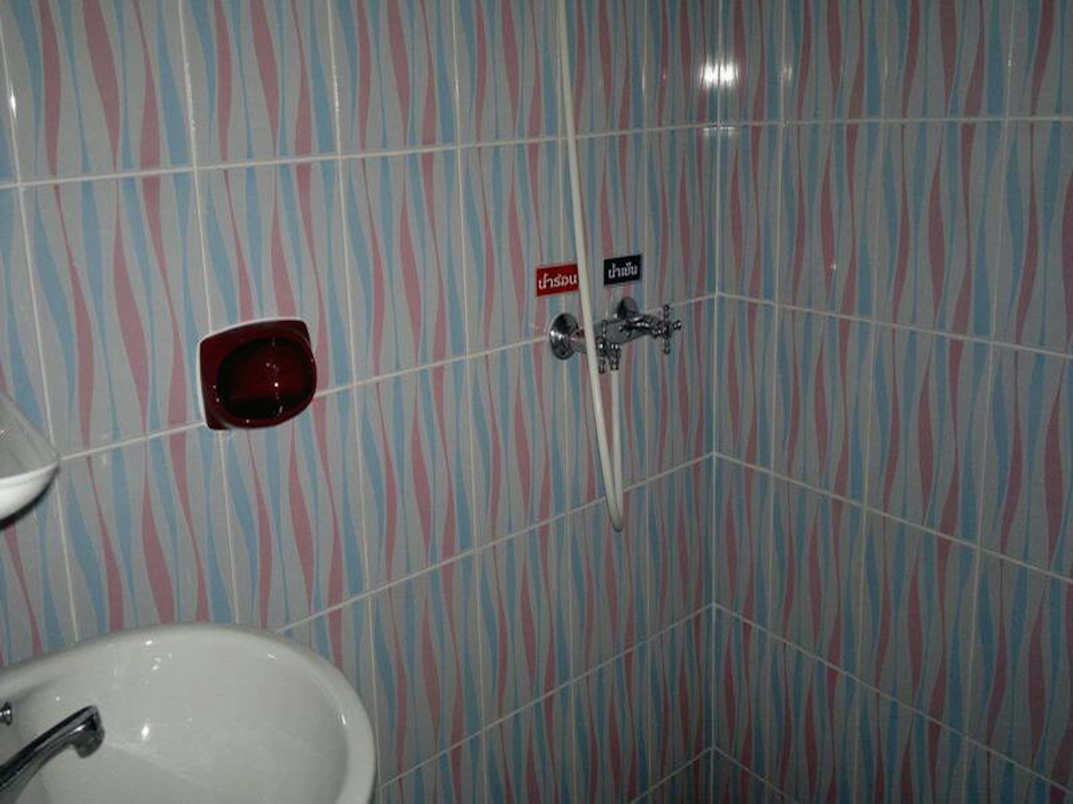 A bathroom with striped tile walls, a white sink, and a shower with a faucet and a red soap dish.