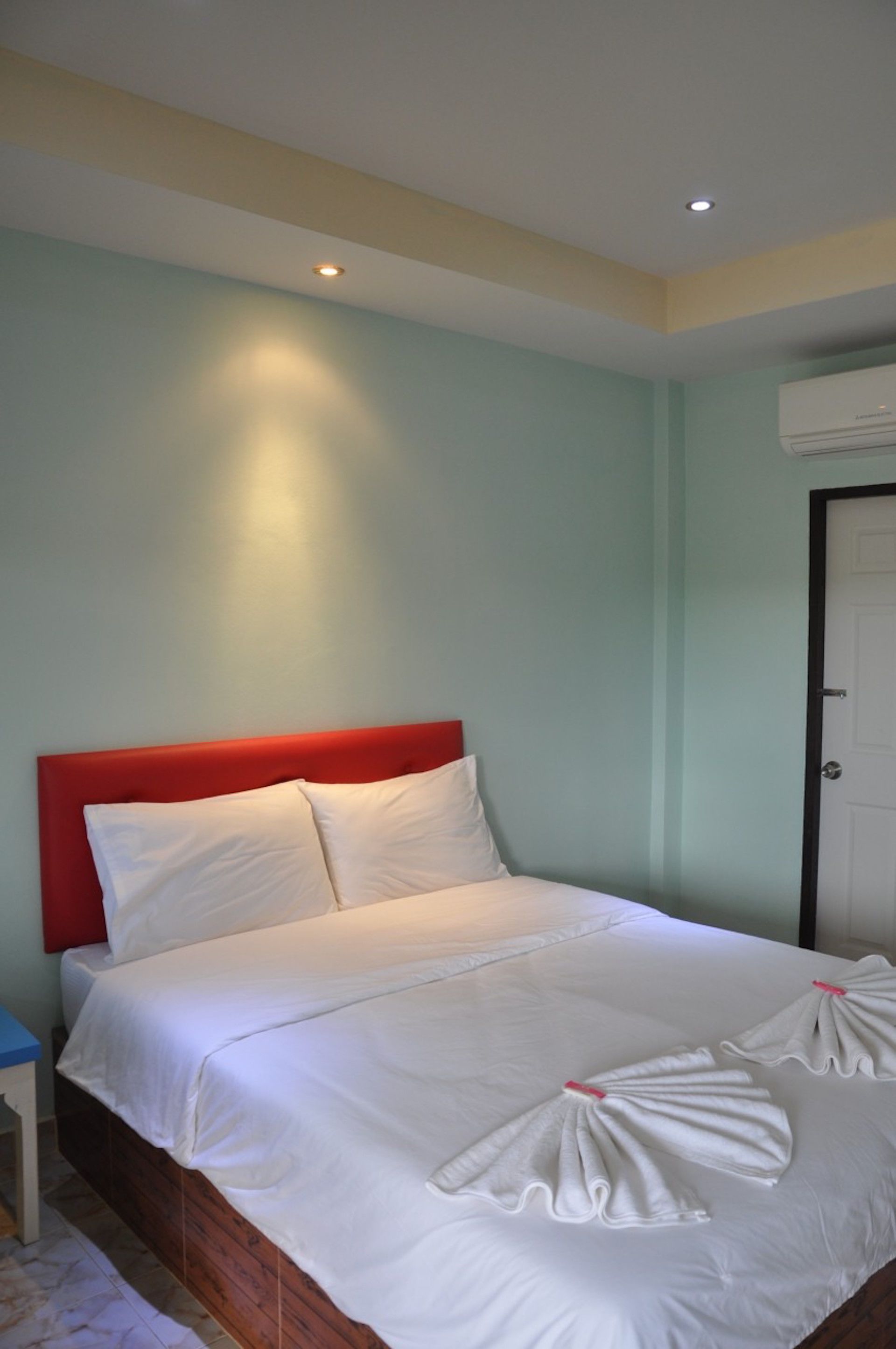 Habitación de hotel con cama, cabecero rojo, ropa de cama blanca y toallas dispuestas sobre la cama.