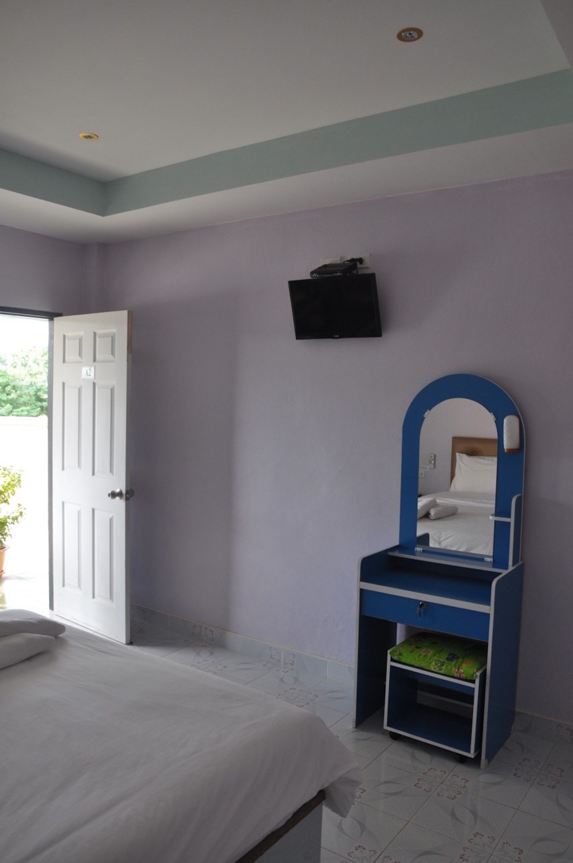 Un dormitorio con cama, un tocador azul con espejo, una puerta y un televisor de pared.