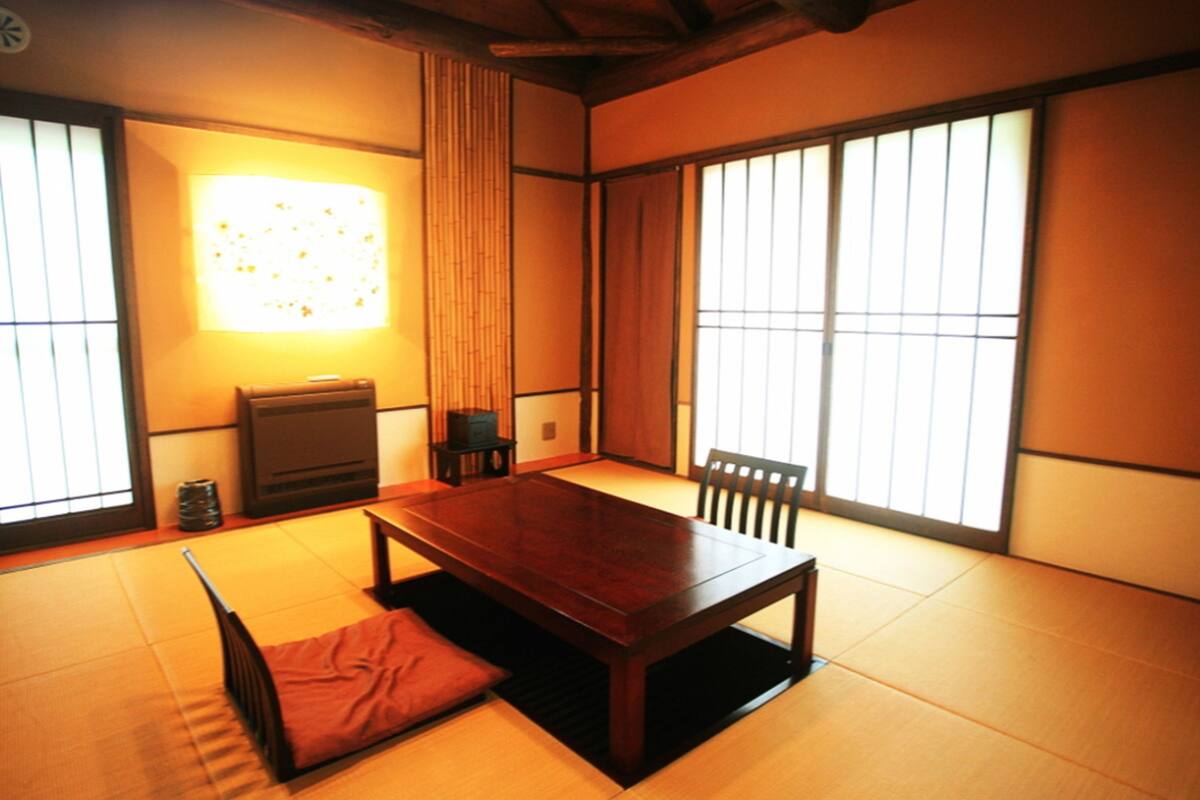 Una tipica stanza giapponese con pavimenti in tatami, un tavolo in legno, una panca bassa in legno e porte scorrevoli.