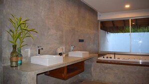 Un baño moderno con dos lavamanos, una bañera amplia y una ventana con vista a la vegetación.