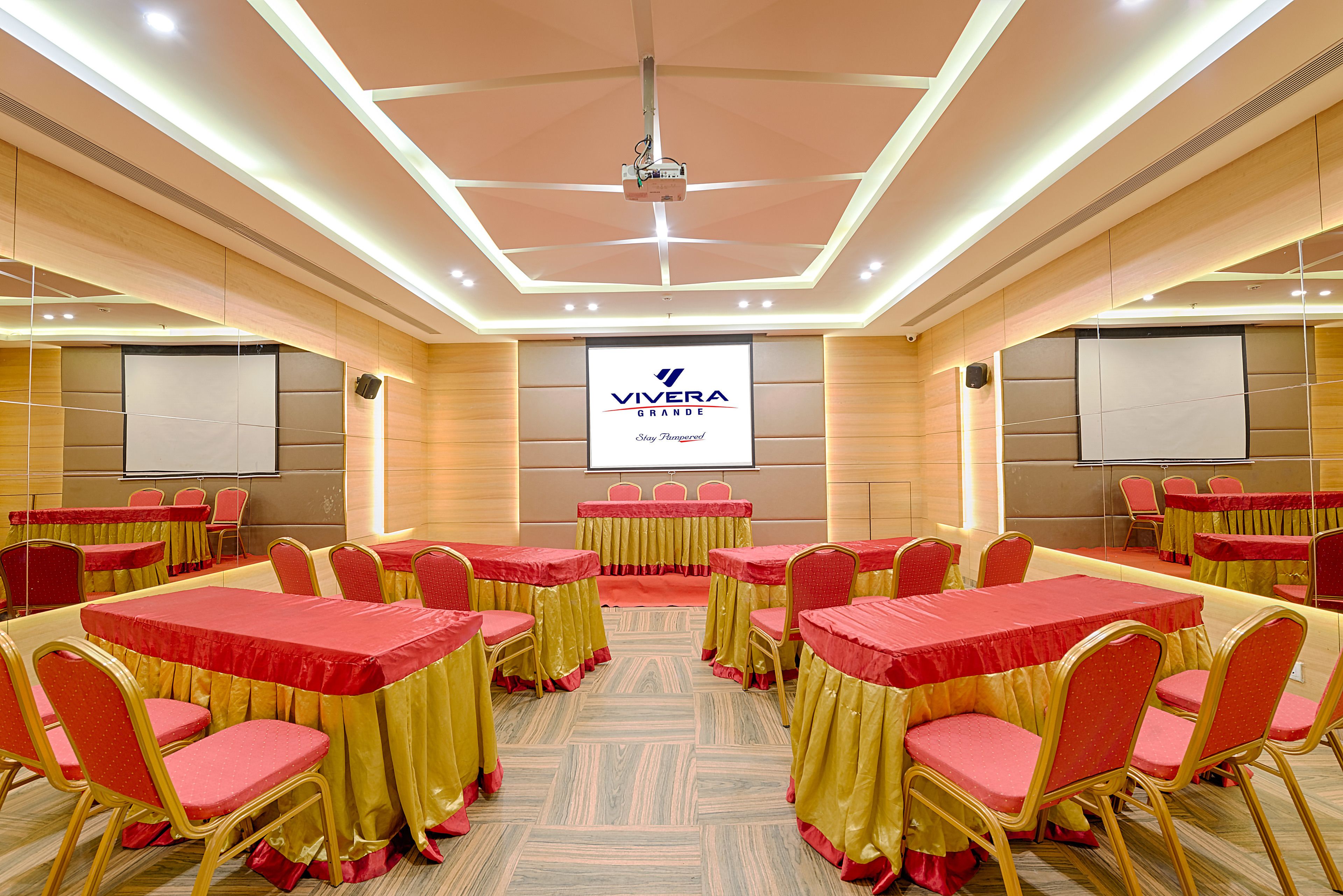 A conference room with tables and chairs, a projector, and a screen displaying the Vivera Grande logo.