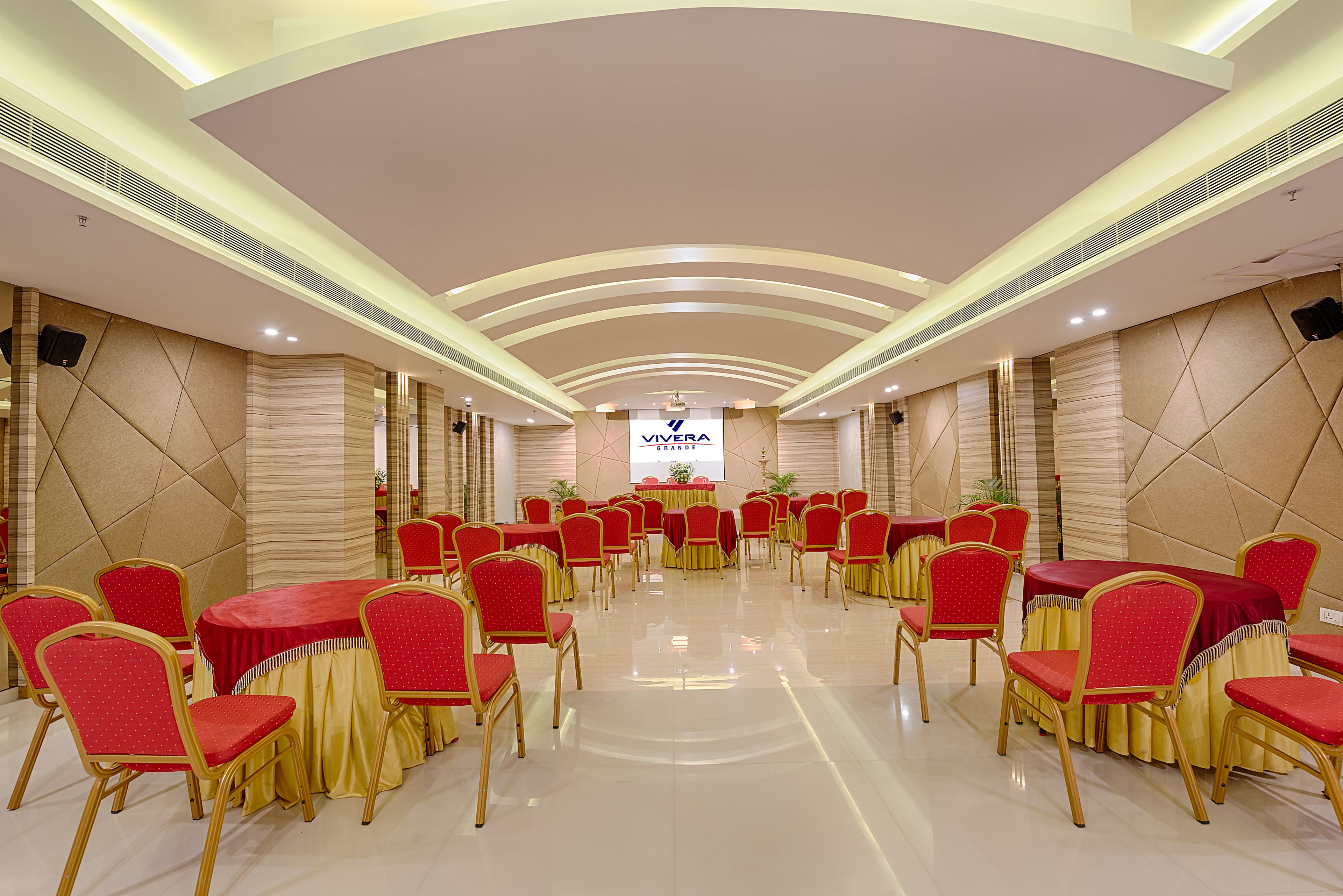 A conference room with round tables and red chairs, a stage with a podium, and a banner reading "Vivera".